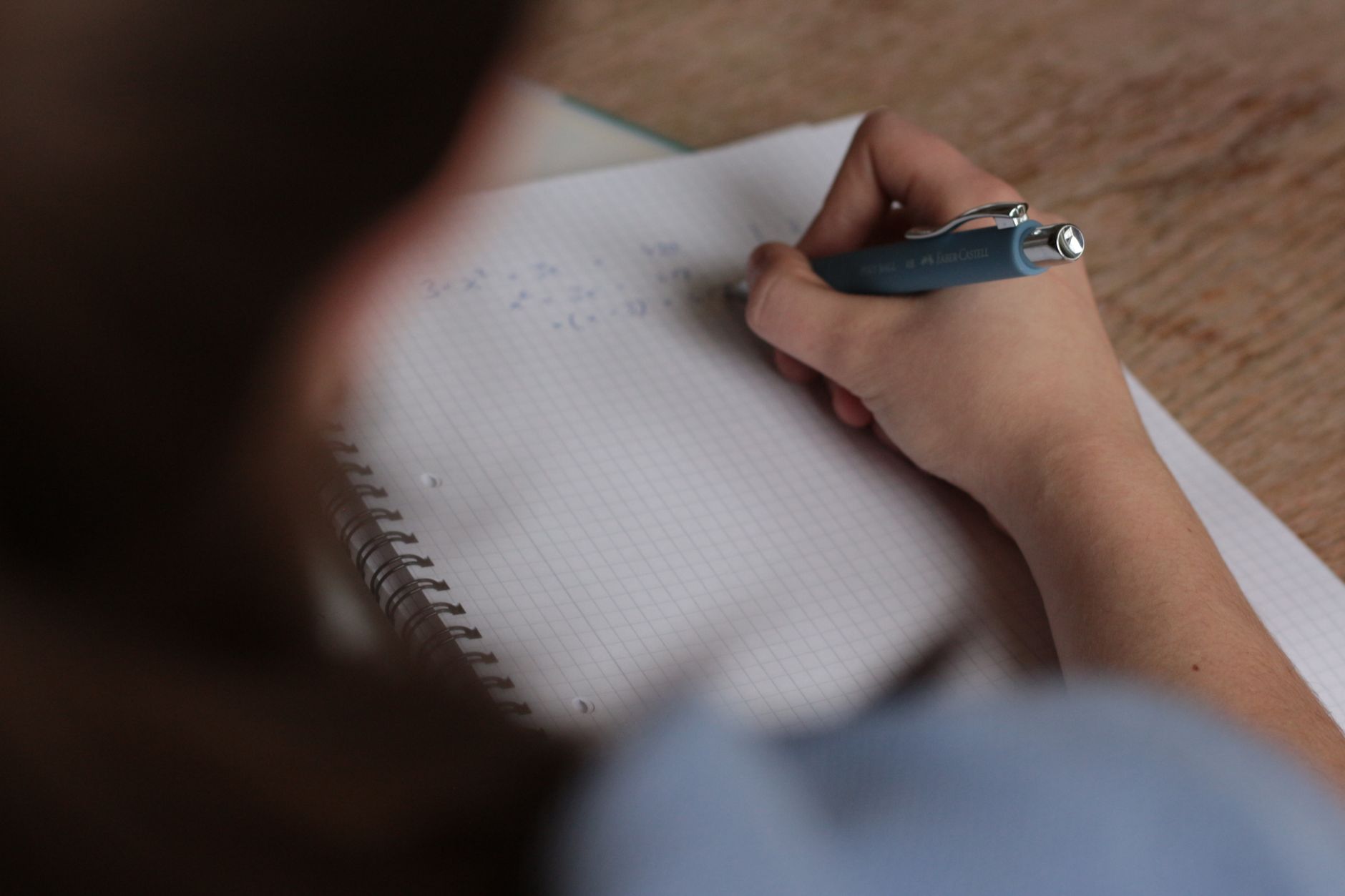 En studerende skriver matematiske noter i en notesbog med pen, fokus på det at studere.